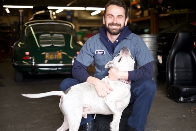 Arndt Voges in a garage, next to a vintage Porsche 356, with a white dog